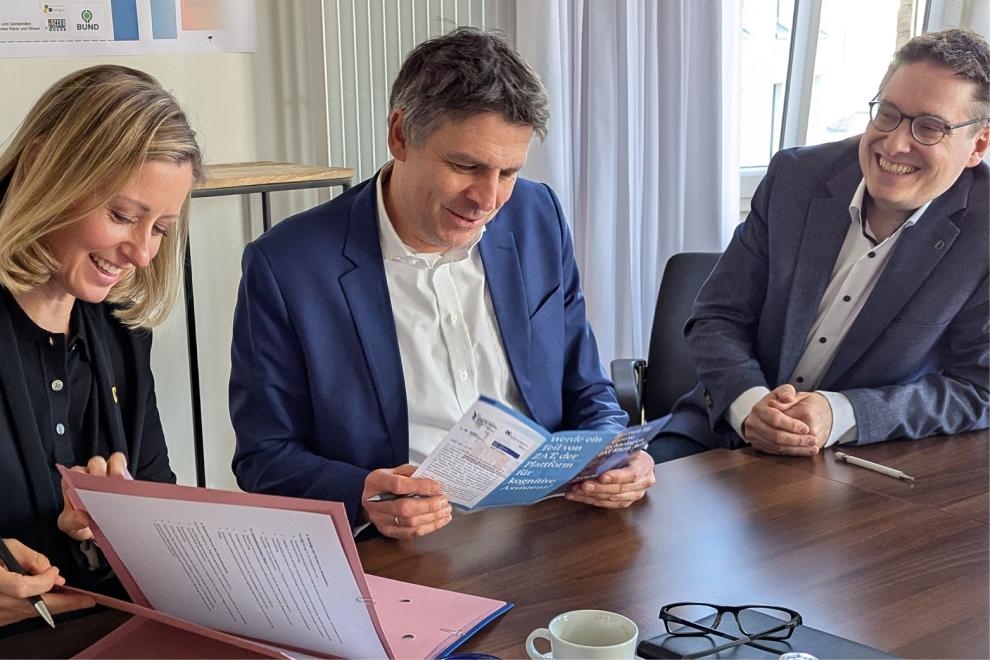 Drei Personen sitzen mit Dokumenten am Tisch