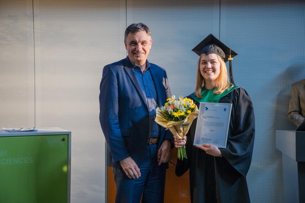 Dr. Wimmer (Mann im Anzug) und Lena Bongers (Frau in Robe) bei der Preisübergabe.